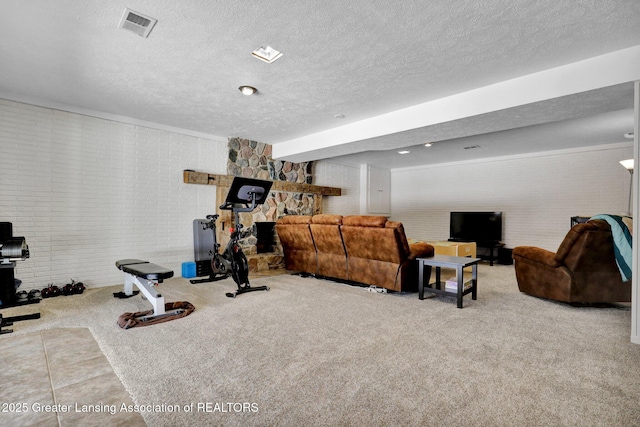 exercise area featuring light colored carpet, brick wall, a stone fireplace, and a textured ceiling