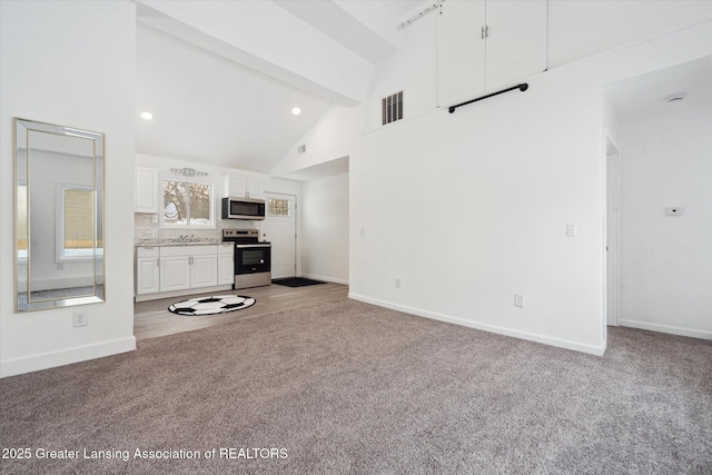 unfurnished living room with light carpet, high vaulted ceiling, and beamed ceiling