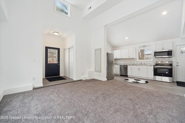 unfurnished living room with a wealth of natural light, light carpet, and high vaulted ceiling