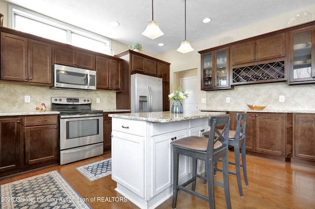 kitchen with hanging light fixtures, light wood-type flooring, stainless steel appliances, and light stone countertops