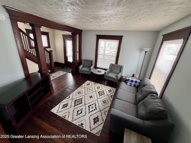 living room with plenty of natural light, dark hardwood / wood-style floors, a textured ceiling, and ornate columns