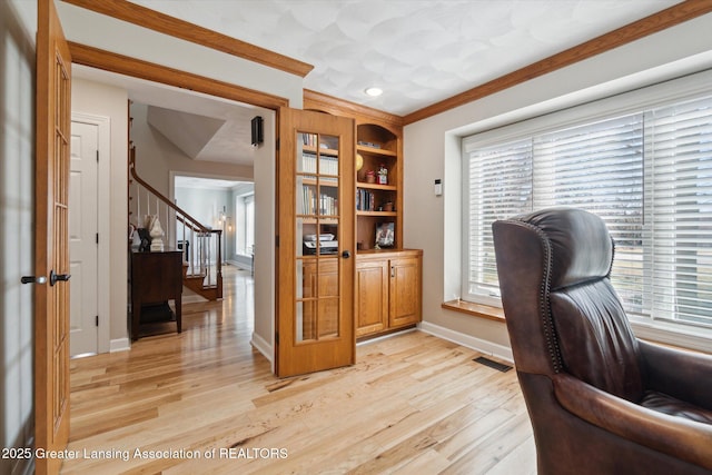 office area with light wood-type flooring, baseboards, visible vents, and crown molding