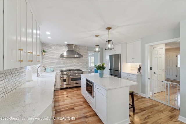 kitchen featuring white cabinetry, wall chimney range hood, light wood finished floors, and appliances with stainless steel finishes