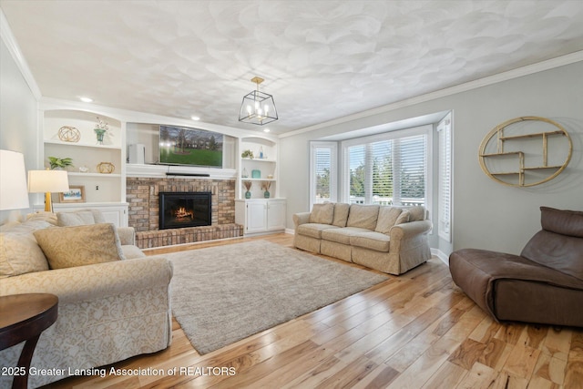 living area with built in features, baseboards, crown molding, a brick fireplace, and light wood-type flooring