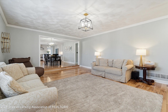 living area featuring visible vents, crown molding, baseboards, a chandelier, and wood finished floors