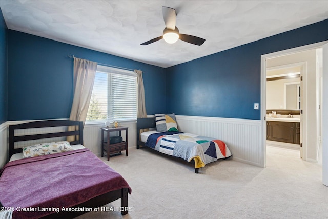 bedroom featuring light carpet, wainscoting, ceiling fan, and a sink