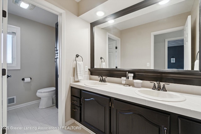 bathroom with double vanity, visible vents, toilet, and a sink