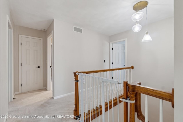 corridor with an upstairs landing, visible vents, baseboards, and carpet floors