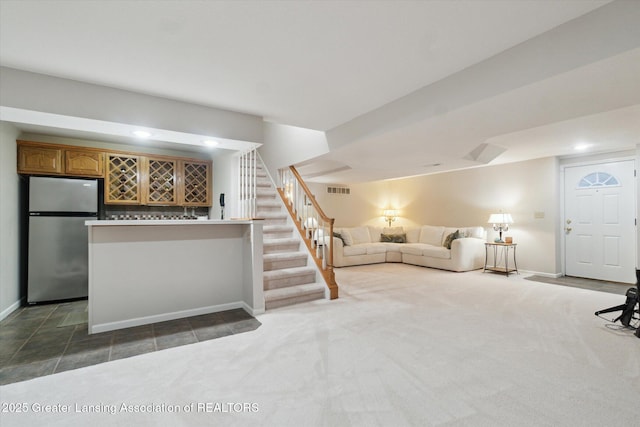 unfurnished living room featuring visible vents, baseboards, a dry bar, stairs, and dark colored carpet