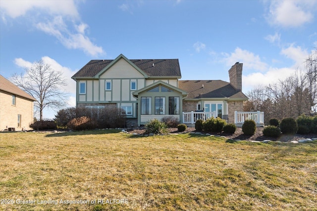 back of property featuring a chimney, a lawn, and a wooden deck