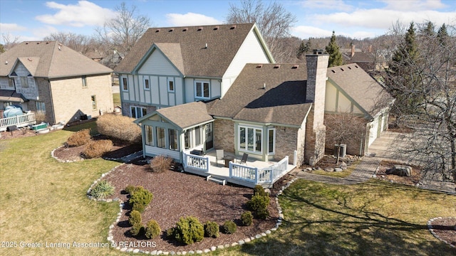 rear view of house featuring a lawn, stone siding, a shingled roof, a sunroom, and a chimney