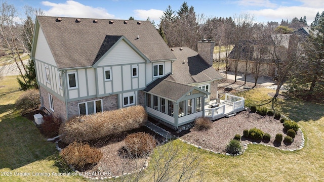 rear view of property featuring stone siding, a chimney, a yard, and a sunroom