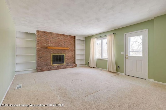 unfurnished living room with a brick fireplace, light carpet, built in features, and a textured ceiling