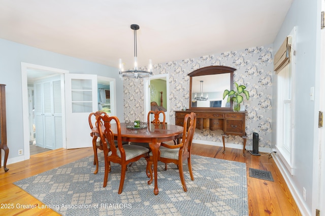 dining space with a chandelier, wood finished floors, visible vents, baseboards, and wallpapered walls