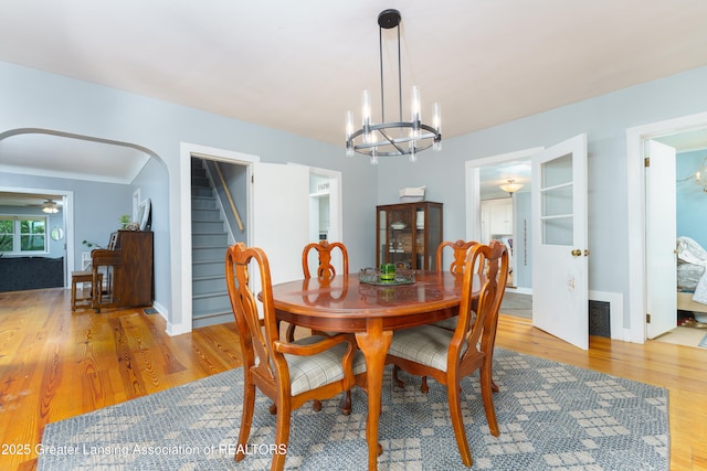 dining space with arched walkways, light wood finished floors, stairs, and visible vents