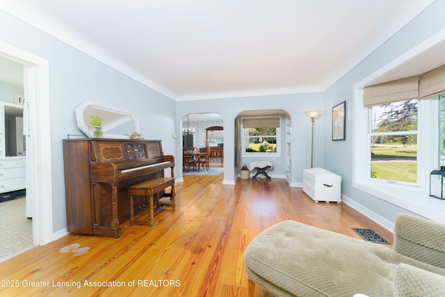 living area featuring light wood finished floors, baseboards, visible vents, and arched walkways