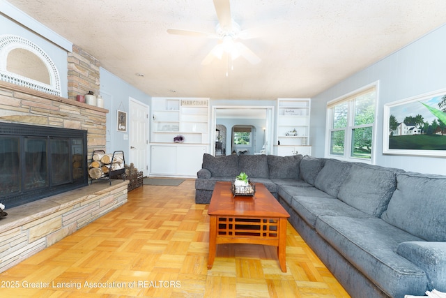 living area with a ceiling fan, arched walkways, a textured ceiling, and a stone fireplace