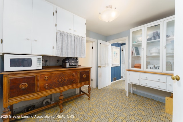 interior space featuring glass insert cabinets, white cabinetry, and white microwave