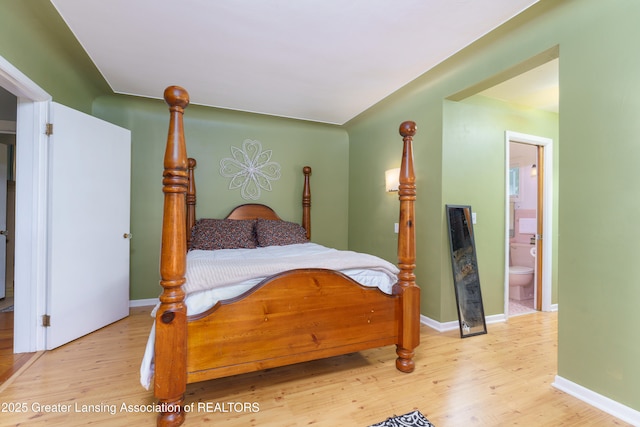 bedroom with ensuite bath, light wood-style flooring, and baseboards