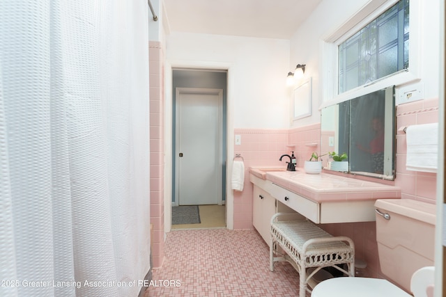 full bathroom with tile walls, a shower with shower curtain, toilet, wainscoting, and vanity