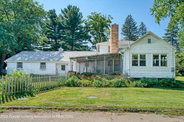 rear view of property with a sunroom, a chimney, fence, and a yard