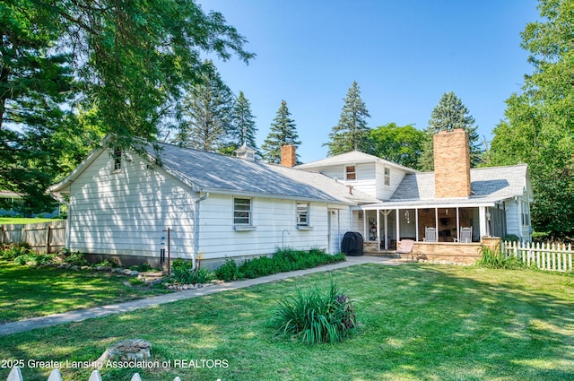 rear view of property with a patio, a lawn, a chimney, and fence