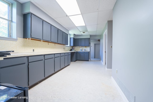 kitchen featuring a paneled ceiling, baseboards, light countertops, and backsplash