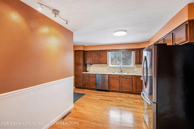 kitchen with sink, tasteful backsplash, a textured ceiling, light wood-type flooring, and stainless steel appliances