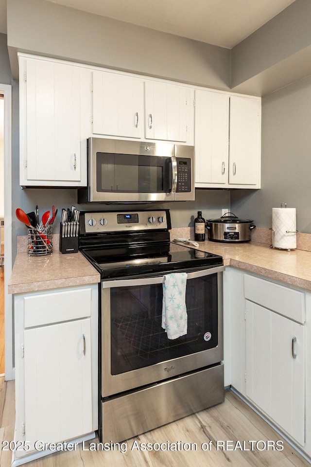 kitchen with stainless steel appliances, white cabinets, and light wood-type flooring