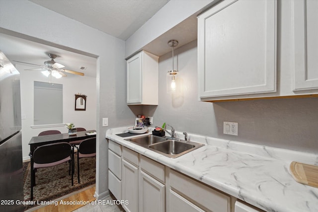 kitchen featuring decorative light fixtures, white cabinetry, sink, light stone counters, and light hardwood / wood-style floors