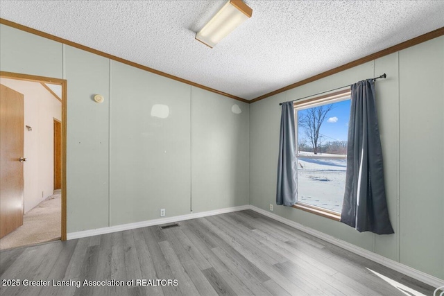 unfurnished room featuring lofted ceiling, crown molding, a textured ceiling, and light wood-type flooring