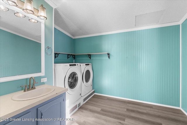 clothes washing area with washing machine and dryer, sink, crown molding, and light wood-type flooring