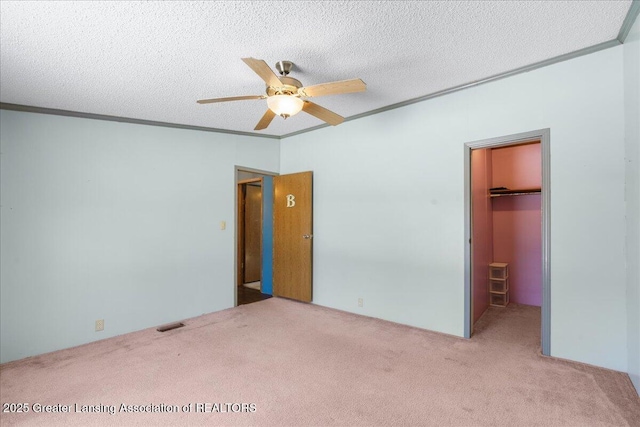 unfurnished bedroom featuring a walk in closet, a textured ceiling, ornamental molding, a closet, and light colored carpet