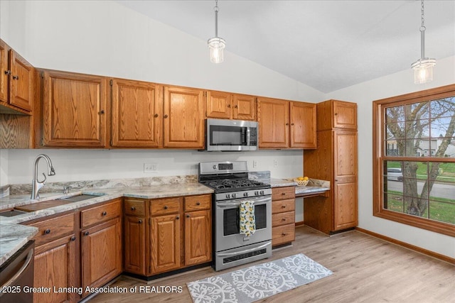 kitchen with vaulted ceiling, sink, hanging light fixtures, stainless steel appliances, and light stone countertops