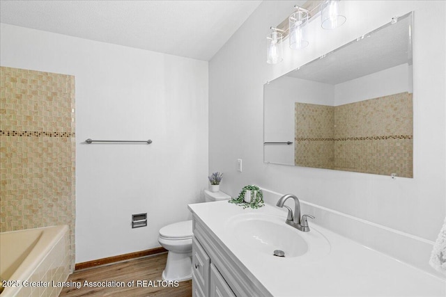 bathroom with wood-type flooring, a relaxing tiled tub, vanity, and toilet