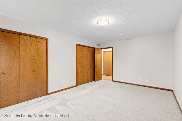 unfurnished bedroom featuring light carpet, two closets, and a textured ceiling