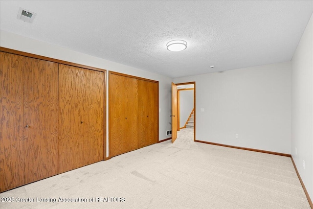 unfurnished bedroom with light carpet, two closets, and a textured ceiling