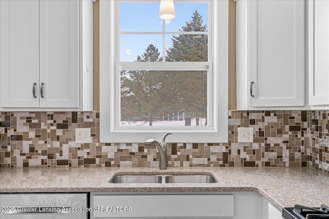 kitchen featuring tasteful backsplash, dishwasher, sink, white cabinets, and light stone counters