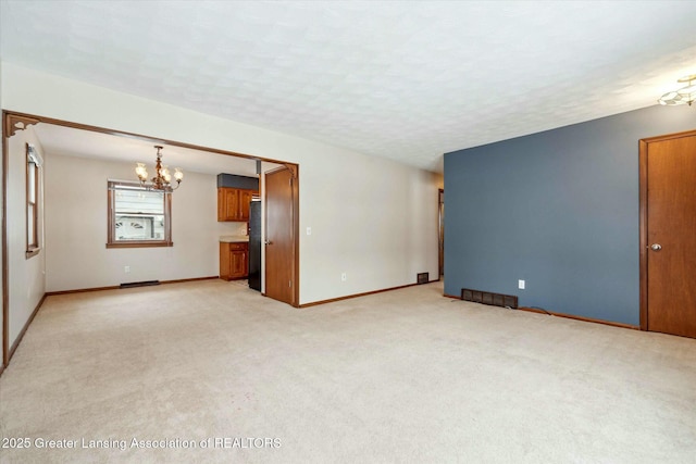 unfurnished living room with an inviting chandelier, light colored carpet, and a textured ceiling