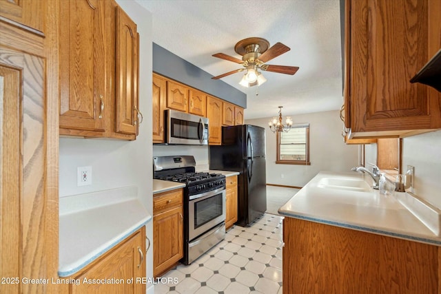 kitchen with sink, decorative light fixtures, a textured ceiling, appliances with stainless steel finishes, and ceiling fan with notable chandelier