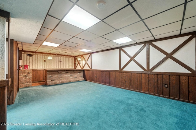 basement with carpet floors, bar, a drop ceiling, and wooden walls