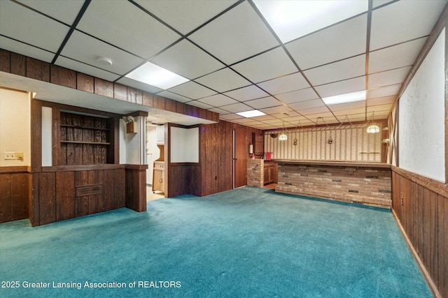 interior space with a drop ceiling, built in features, carpet, and wood walls