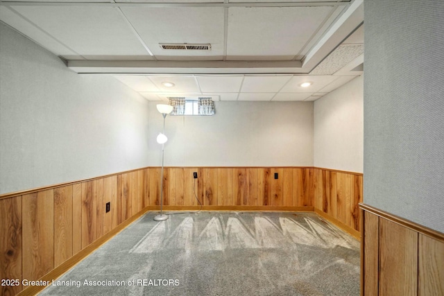 carpeted spare room featuring a paneled ceiling and wood walls