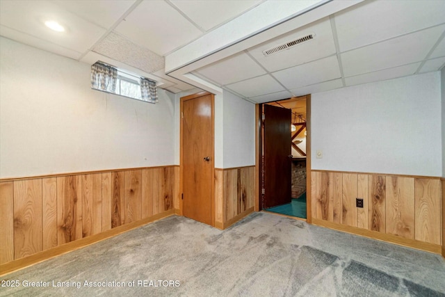 basement featuring a paneled ceiling, light carpet, and wood walls