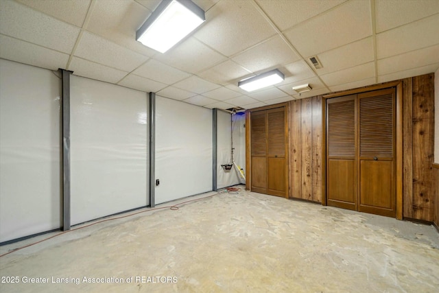 basement with a drop ceiling and wooden walls