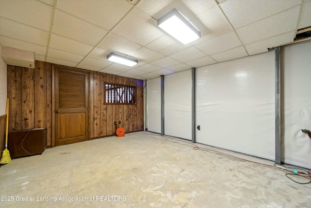 basement featuring a drop ceiling and wood walls