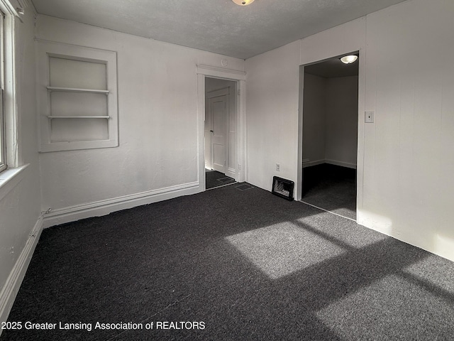 empty room featuring built in shelves, a textured ceiling, and dark colored carpet