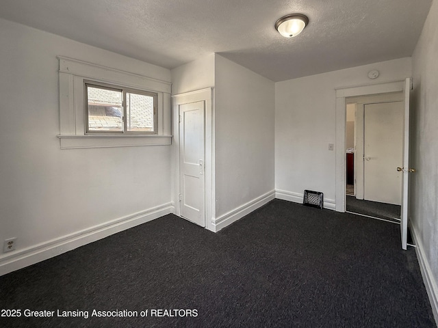 empty room with a textured ceiling and dark colored carpet