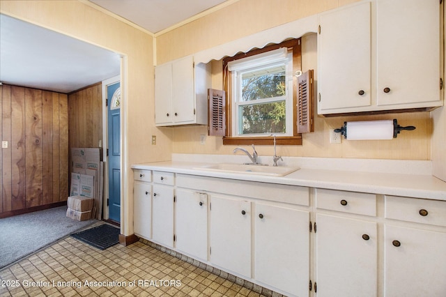 kitchen with ornamental molding, wooden walls, sink, and white cabinets