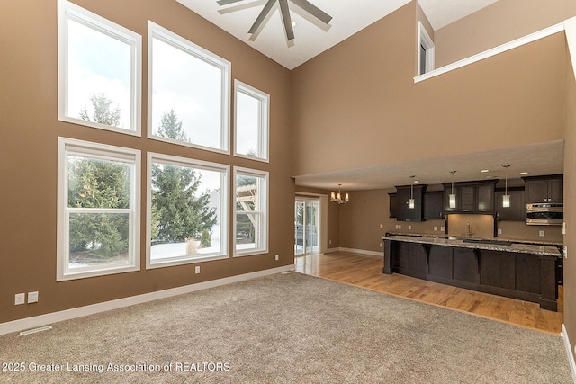 unfurnished living room featuring ceiling fan with notable chandelier, light colored carpet, and high vaulted ceiling